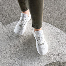 wit Persoon draagt witte Barfuß-leguano® sneakers op een grijze vloer.