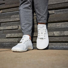 wit Persoon in grijze joggingbroek staat voor een stenen muur met witte sneakers.