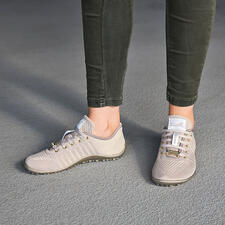 goud Persoon draagt beige Barfuß-leguano® sneaker op een grijze vloer.