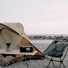 zwart Digitale survivalradio op een tafel op het strand met een tent op de achtergrond.