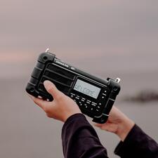 zwart Persoon houdt digitale survivalradio omhoog terwijl hij/zij op het strand staat.