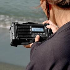 zwart Persoon houdt digitale survivalradio op het strand en kijkt naar het ontvangst.