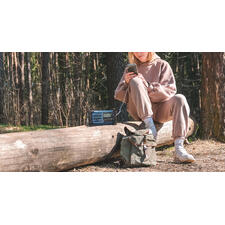 blauw Vrouw in beige kleding zit op een stam met een radio en een rugzak.