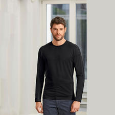 lange mouw, met ronde hals, zwart Man in zwart Sunspel-shirt, staat in een kamer met heldere ramen.