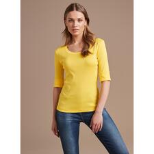 geel Vrouw met een geel langemouwen shirt en jeans, voor een neutrale achtergrond.