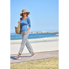 jeansblauw Vrouw in blauwe blouse en zonnehoed die over het strand wandelt.