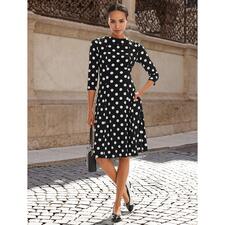 creme/zwart lak Vrouw in een stippenjurk staat op straat, glimlachend.