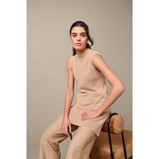 slip-over Junghans 1954 lange pullover in beige, model zit op een kruk.