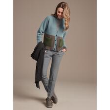 taupe Vrouw in groene cardigan met Chaaya schapenwollen sneakers op een bruine achtergrond.