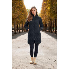 donkerblauw Vrouw in een zwarte gewatteerde jas staat voor de achtergrond van een park.