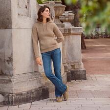 Silver Suki bootcutjeans Vrouw in een kameelhaar hoodie leunt tegen een zuil buitenshuis