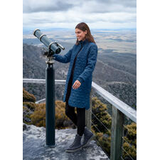 royalblauw Vrouw in koninklijk blauwe gewatteerde jas, staand bij een telescoop.