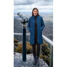 royalblauw Vrouw in een koningsblauwe gewatteerde jas op een uitkijkpunt met telescoop.