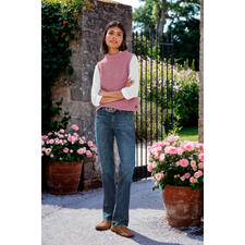 Silver Suki bootcutjeans Vrouw in een roze wool vest over een wit longsleeve, staat aan een bloeiende poort.