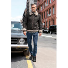 OCONI B3-pilotenjack van lamsvacht Man in een bruine lammy-pilotenjack staat voor een oldtimer in de stad.