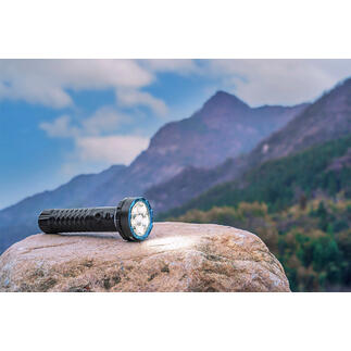 Bidirectionele 5000 lumen zaklamp op een steen met berglandschap op de achtergrond.