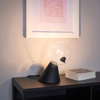 Tafel lamp Satellite met heldere glazen bol en zwarte voet op een plank.