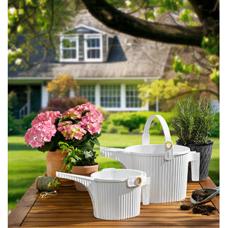 Twee gieters in wit en bloemen op een tafel in de tuin