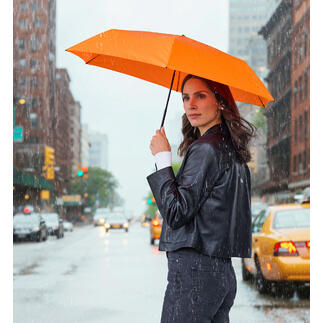 Vrouw houdt een oranje taschenscherm in de regen, staand op de straat.