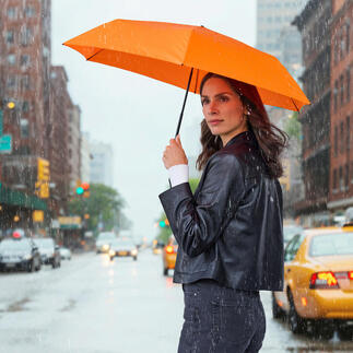Vrouw houdt een oranje taschenscherm in de regen, staand op de straat.