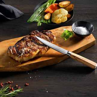 Damast steakmes op houten snijplank met gegrild steak en groenten.