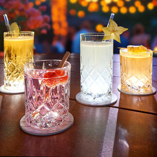 Vier verlichte glazen op een tafel met LED-onderzetters, ideaal voor een feestelijke sfeer.