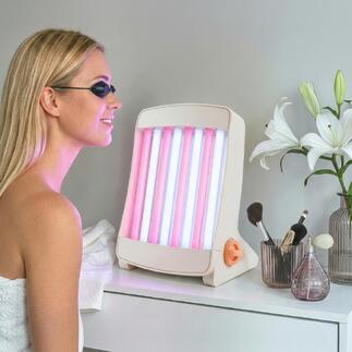 Gezichtsbruiner met roze en blauwe lampen, staat op een tafel naast cosmetica.