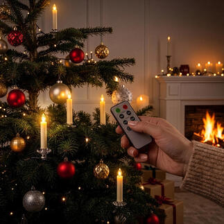 Een hand die een afstandsbediening voor LED echte wax kerstkaarsen aan de kerstboom vasthoudt.