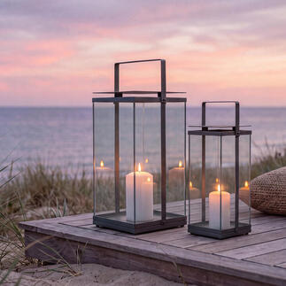 Twee design-laternen op een houten terras aan het strand bij zonsondergang.