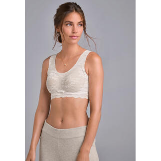 Vrouw in crèmekleurige kanten bralette, glimlachend voor een neutrale achtergrond.