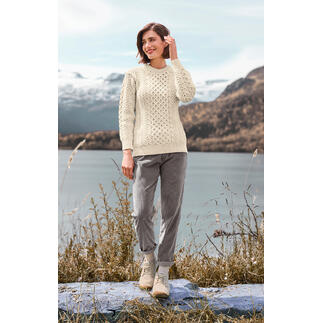 Vrouw in een wolwit Merino-Aran sweater aan het water met uitzicht op bergen
