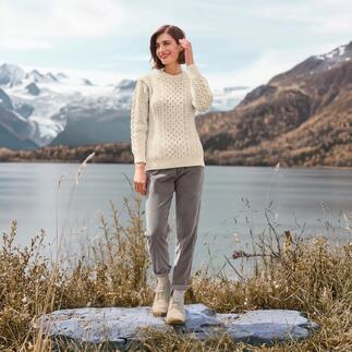 Vrouw in een wolwit Merino-Aran sweater aan het water met uitzicht op bergen