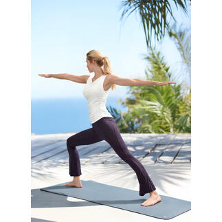 Vrouw in yogapose draagt een wit waterfall-shirt en yogabroeken op een houten terras buiten.