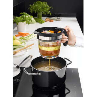 Hand met een zeef giet groentebouillon in een pan, terwijl een keuken op de achtergrond zichtbaar is.