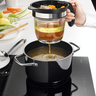 Hand met een zeef giet groentebouillon in een pan, terwijl een keuken op de achtergrond zichtbaar is.