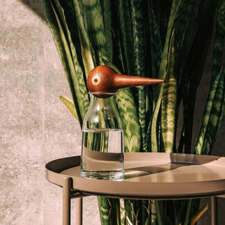 Glas water met houten vogelvormige waterdispenser op een tafel.