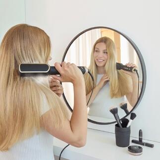 Vrouw met ionen-haarborstel voor een spiegel in een moderne ruimte.