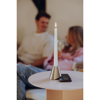 Kaars in metalen houder op tafel, achtergrond met mensen.