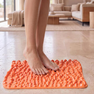 goFit voetreflexmat in feloranje, op een lichte vloer met voeten erop.