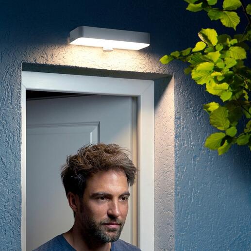 Man staat onder een buitenwandlamp bij de deur.
