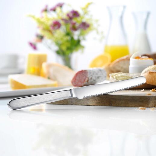 Broodmes van roestvrij staal op een tafel met brood en bloemen.