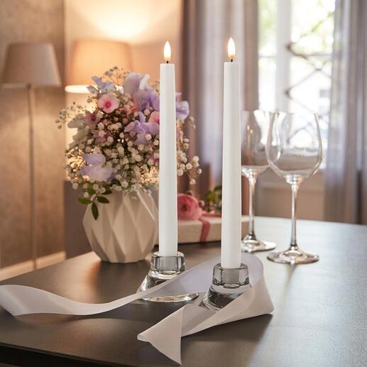 Twee LED-stabkaarsen in een decoratieve omgeving naast bloemen.