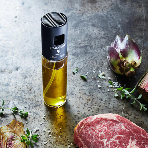 Olie-spuitfles met filter naast rauwe steak en kunstbloemen op een rustieke tafel.