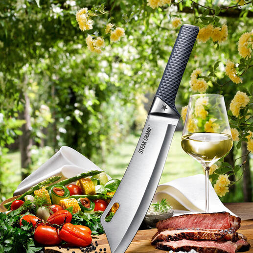 SteakChamp koksmes van bovenaf, omringd door groenten en vlees op een snijplank.