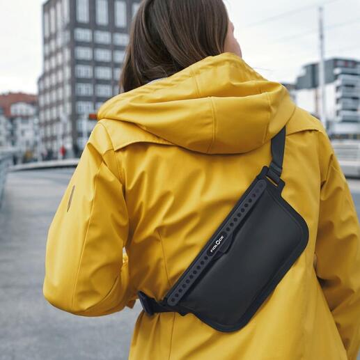 Vrouw in een gele jas draagt een zwarte crossbody tas over haar schouder.