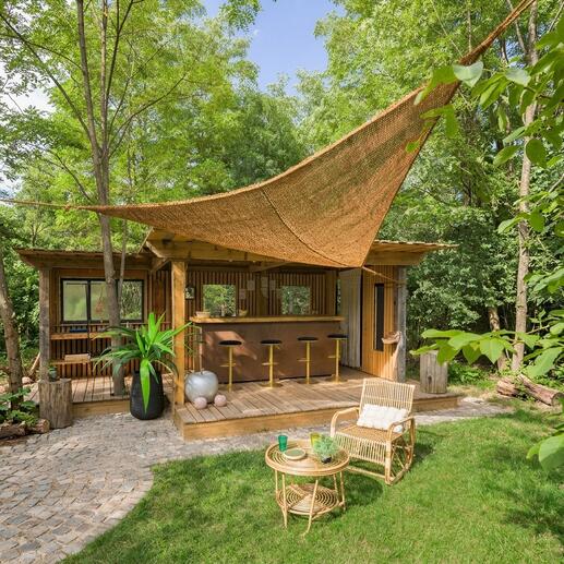 Zonnescherm van kokosvezels boven een houten terras met barkrukken.