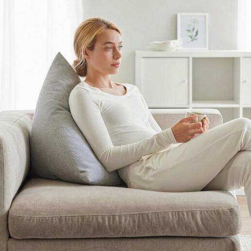 Vrouw met een grijs rugkussen die ontspannen op een bank zit.