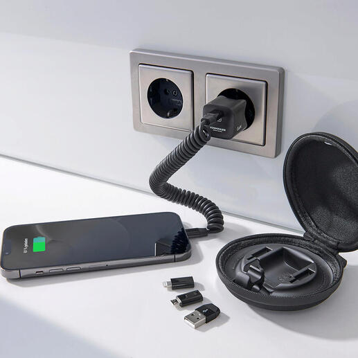 Smartphone, oplader en accessoires op een tafel, omgeven door een wandcontactdoos.