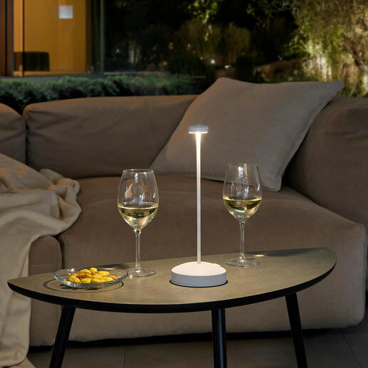 Design tafellamp met batterij op een tafel, omringd door wijnglazen en snacks.