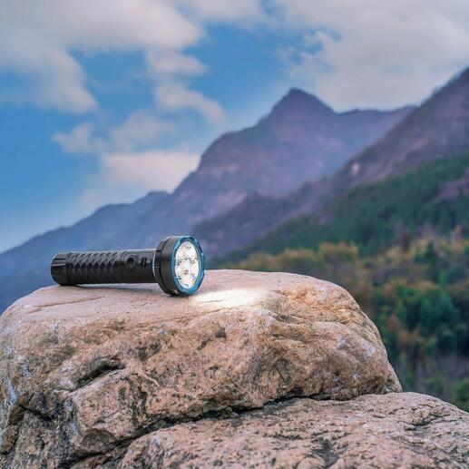 Bidirectionele 5000 lumen zaklamp op een steen met berglandschap op de achtergrond.